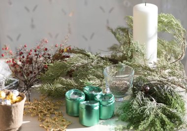 Pencerenin kenarındaki bir masada mumlar, kozalaklı dallar, böğürtlenler ve altın kar taneleri