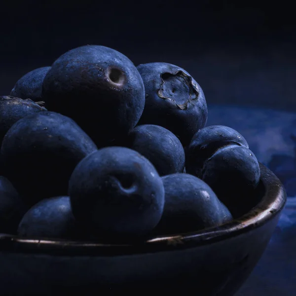 Small bowl of freshly picked blueberries in dark stone bowl on b
