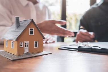 Emlakçı ve müşteriyle ev modeli satın alma, sigorta ya da kredi alma ya da emlak ya da mülkiyet sözleşmesi hakkında tartışıyor.