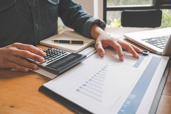 Close-up of businessman hand using calculator to calculate business data, accountancy document at home office.