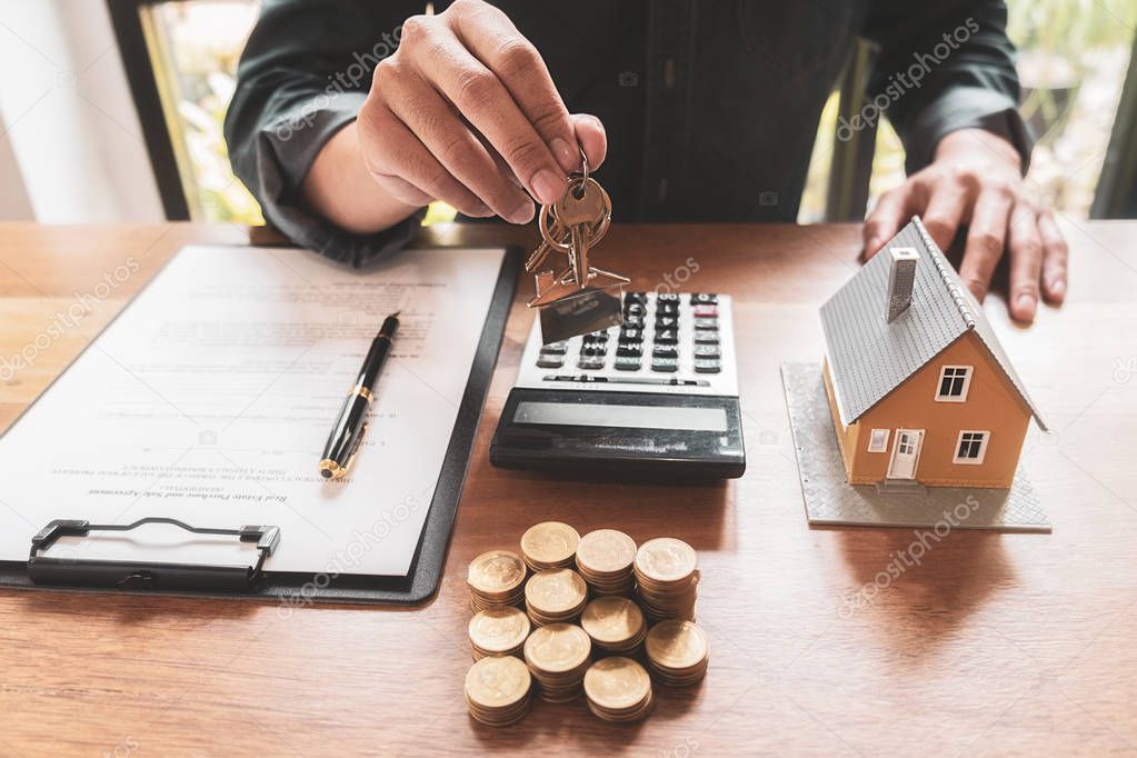 Real estate agent holding a key and asking costumer for contract to buy, get insurance or loan real estate or property.