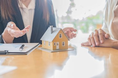 Emlakçı ve müşteriyle ev modeli satın alma, sigorta ya da kredi alma ya da emlak ya da mülkiyet sözleşmesi hakkında tartışıyor.