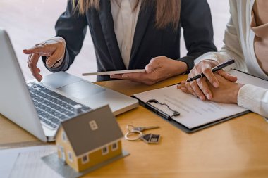 Emlakçı ve müşteriyle ev modeli satın alma, sigorta ya da kredi alma ya da emlak ya da mülkiyet sözleşmesi hakkında tartışıyor.