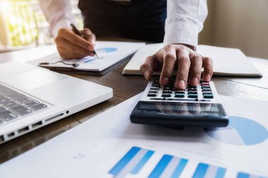 İş adamlarının iş verilerini hesaplamak için hesap makinesi kullanarak yakın plan çekimleri, merkez ofiste muhasebe belgesi.