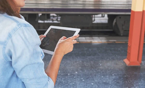 Woman traveler tourist using tablet at train station. Traditional train for transportation.