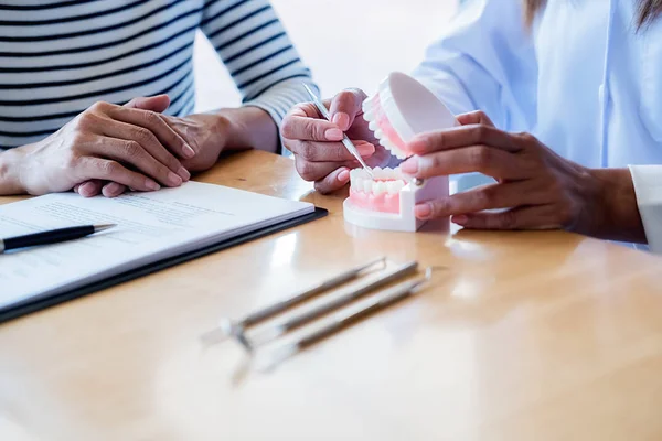 Dentista mostrando e explicando o tratamento da doença dentária para o paciente usando dentadura modelo e ferramenta espelho explorador dentes no consultório de clínica odontológica. Conceito de saúde . — Fotografia de Stock