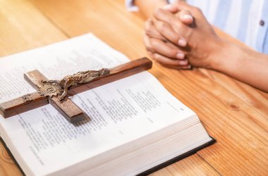 Hıristiyan kadın kutsal İncil ve ahşap haç üzerinde el ele dua ediyor. Kadınlar, daha iyi bir hayat için Tanrı 'ya dua eder ve iyiliğe inanır..