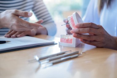 Diş hekimi, diş macunu ve dişçi muayenehanesindeki ayna aletini kullanarak hastaya diş hastalıkları tedavisini gösteriyor ve açıklıyor. Sağlık hizmetleri kavramı.