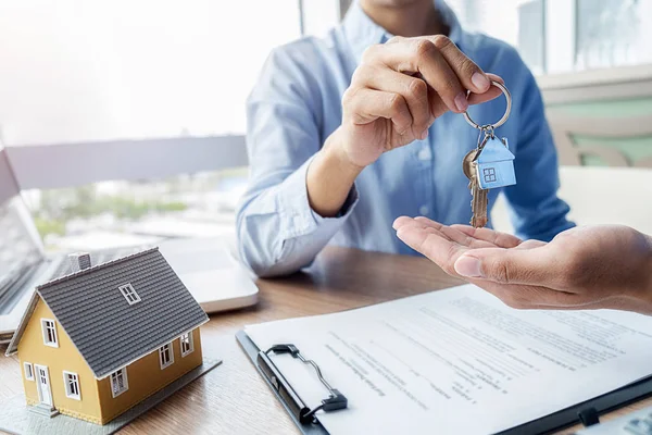 Real estate agent holding a key and asking costumer for contract to buy, get insurance or loan real estate or property.