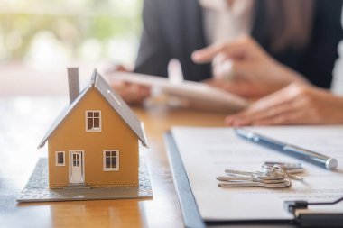 Emlakçı ve müşteriyle ev modeli satın alma, sigorta ya da kredi alma ya da emlak ya da mülkiyet sözleşmesi hakkında tartışıyor.
