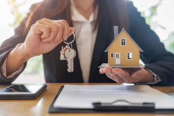 Real estate agent holding a key and asking costumer for contract to buy, get insurance or loan real estate or property.