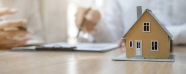 Emlakçı ve müşteriyle ev modeli satın alma, sigorta ya da kredi alma ya da emlak ya da mülkiyet sözleşmesi hakkında tartışıyor.