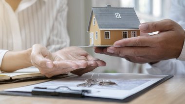 Emlakçı ve müşteriyle ev modeli satın alma, sigorta ya da kredi alma ya da emlak ya da mülkiyet sözleşmesi hakkında tartışıyor.