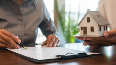 Emlakçı ve müşteriyle ev modeli satın alma, sigorta ya da kredi alma ya da emlak ya da mülkiyet sözleşmesi hakkında tartışıyor.