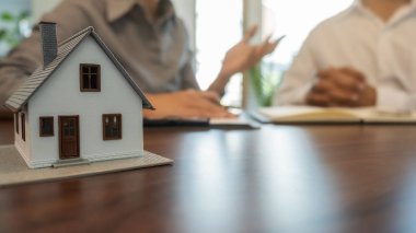 Emlakçı ve müşteriyle ev modeli satın alma, sigorta ya da kredi alma ya da emlak ya da mülkiyet sözleşmesi hakkında tartışıyor.