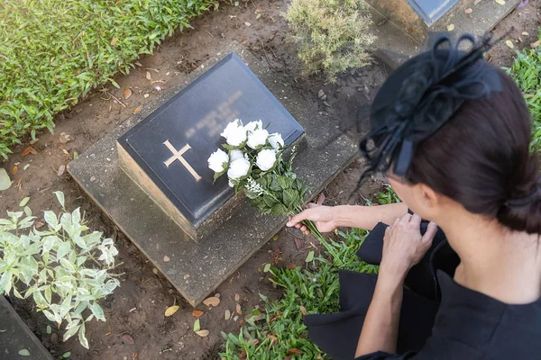 Gyászoló fiatal nő fehér virágokat fektet a családja sírjára a gyönyörű zöld temetőben.. — Stock Fotó
