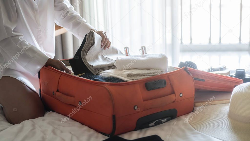 Preparation for vacation or travel. Happiness young woman packing a clothes and stuff into opened suitcase on bed.