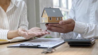 Emlakçı ve müşteriyle ev modeli satın alma, sigorta ya da kredi alma ya da emlak ya da mülkiyet sözleşmesi hakkında tartışıyor.