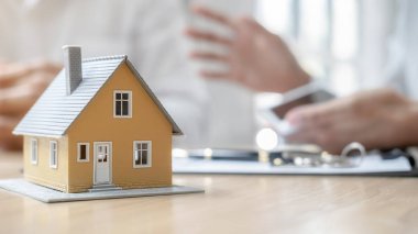 Emlakçı ve müşteriyle ev modeli satın alma, sigorta ya da kredi alma ya da emlak ya da mülkiyet sözleşmesi hakkında tartışıyor.