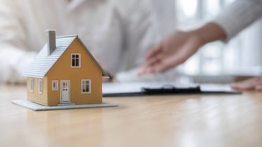 Emlakçı ve müşteriyle ev modeli satın alma, sigorta ya da kredi alma ya da emlak ya da mülkiyet sözleşmesi hakkında tartışıyor.