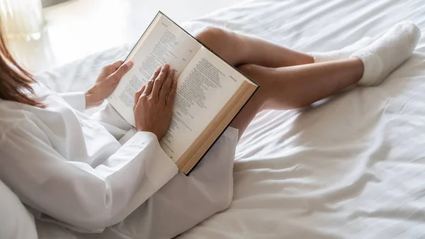 Ázsiai nő olvas egy könyvet az ágyon után kelni reggel puha reggeli fény. Reggeli életmód koncepció. — Stock Fotó