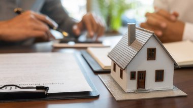 Emlakçı ve müşteriyle ev modeli satın alma, sigorta ya da kredi alma ya da emlak ya da mülkiyet sözleşmesi hakkında tartışıyor.