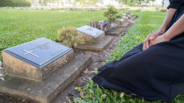 Mourning young woman kneeling at her family grave in beautiful green cemetery. Mourning concept. clipart