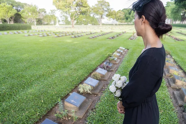 追悼若いです女性ホワイト花を保持彼女の家族の墓で彼女の美しい緑の墓地 — ストック写真