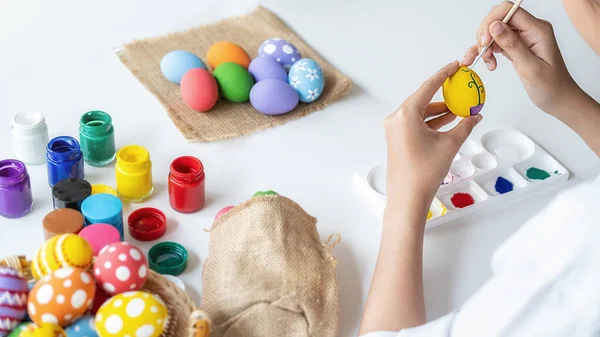 Happy Asian woman painting eggs for Eastertime at home. Family preparing for Easter.