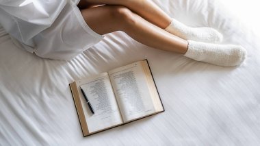 Asyalı bir kadın, sabah uyanıp sabah ışıklarıyla yatakta kitap okuyor. Sabah yaşam tarzı konsepti.