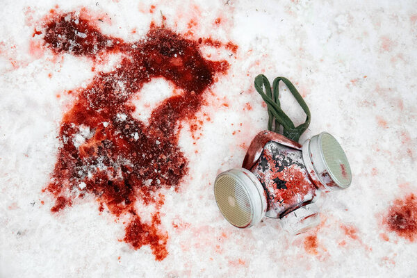 Personal protective equipment gas mask lies in the snow in a puddle of blood