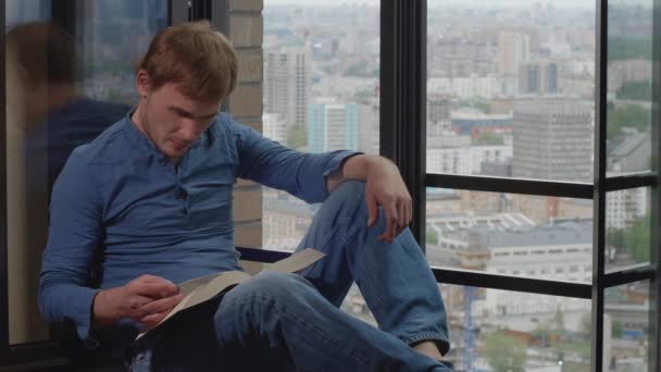 Joven Hombre Caucásico Sentado Alféizar Ventana Lee Libro Ríe Vuelta — Vídeo de stock