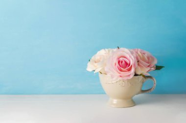 Yapay pembe gül çiçekleri beyaz ve mavi arka planda klasik tonda eski moda bardaklarda.