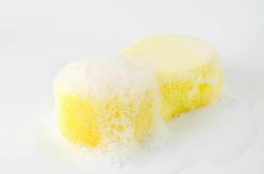 Beyaz arka planda sabunlu ve köpüklü sarı süngeri kapat