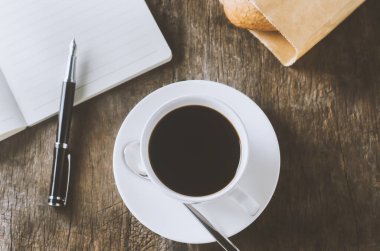 Beyaz defter ve beyaz kalemle beyaz kahve ve ahşap masa üzerinde antika ve canlı tonda bir kalem.