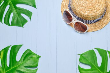 Mavi ahşap zemin üzerinde beyaz güneş gözlüklü hasır şapka yeşil yapraklı, yaz arkaplanı