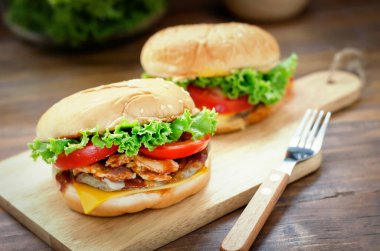 Ev yapımı peynirli burger, ızgara domuz pastırması ve taze sebze, domates ve marul dilimleri ahşap tahtada.