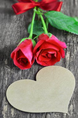Kalp şeklinde boş kahverengi tebrik kartı ve ahşap arka planda kırmızı gül buketi, Sevgililer Günü gülleri
