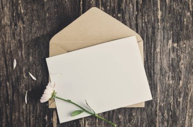 Kahverengi zarf ile boş beyaz tebrik kartı ve solmuş anne çiçekleri eski ve canlı tonda ahşap masada.