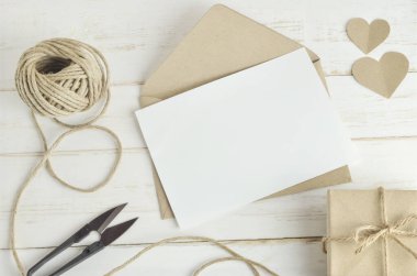 Kahverengi zarf ve eski ahşap masa üzerinde el yapımı hediye kutusuyla boş beyaz tebrik kartı.