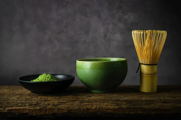 Japanese matcha green tea and matcha green tea powder at homemade clay bowl with bamboo whisk on wooden table with vignette tone