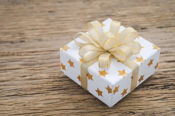Close up of white gif box with golden star pattern and gold ribbon bow on wooden background - Christmas background
