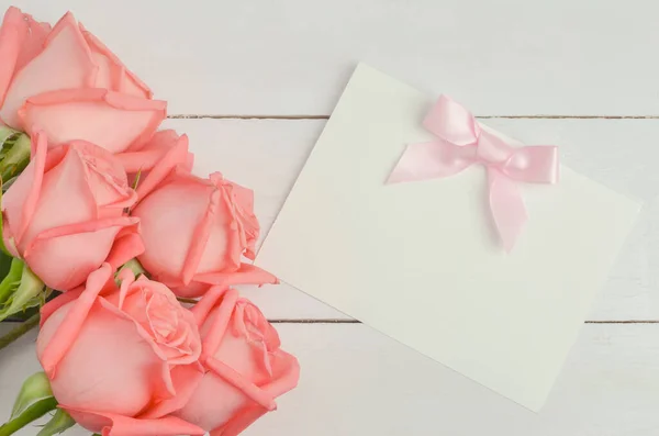 Blank greeting card with pink ribbon bow and pink rose flowers on white wooden background with soft vintage tone, Valentine rose and card