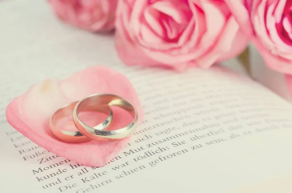 粉色玫瑰花瓣上的金戒指 粉色玫瑰花束 开着的书 带着复古的色调 结婚戒指 — 图库照片