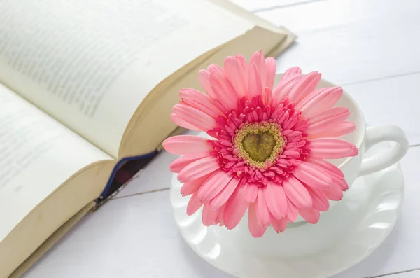 ピンクのガーベラデイジーの花と白いコーヒーカップのクローズアップは 柔らかいヴィンテージトーンで本を開きます — ストック写真