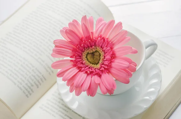 ピンクのガーベラデイジーの花と白いコーヒーカップのクローズアップは 柔らかいヴィンテージトーンで本を開きます — ストック写真