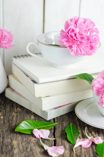 白茶杯のピンクのパステルカーネーションの花や木のテーブルの上の書籍の山の花瓶 — ストック写真