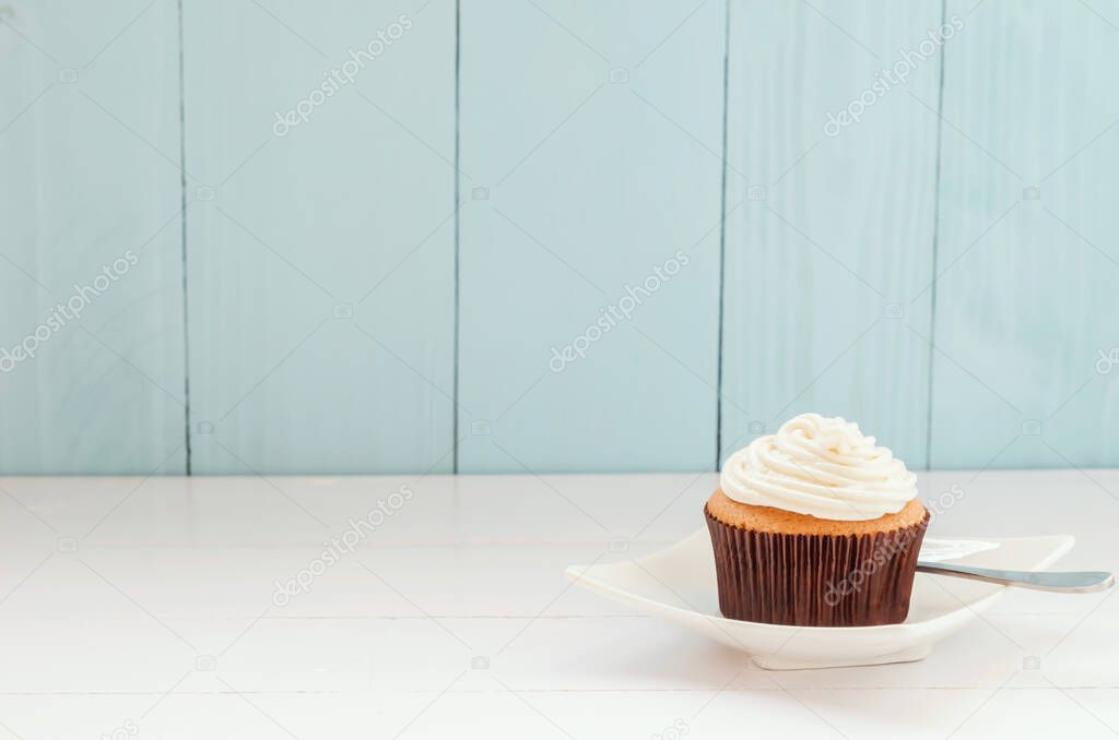 Vanilla cupcake at white dish on white and blue wooden background with soft vintage tone