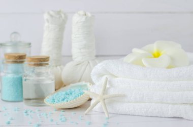 Plumeria çiçekli sabun ve aromaterapi spa aletleri, hindistan cevizi yağı, mavi aroma spa tuzu, bitkisel kompres topları, deniz kabukları, beyaz ahşap zemin üzerinde deniz yıldızı.