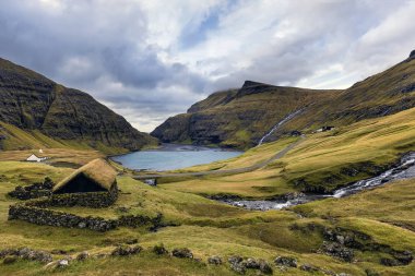 Saksun köyü ve göl kenarının kumlu kıyıları. Göl mavimsi ve dramatik bulutlar. Island Streymoy, Faroe Adaları. Avrupa